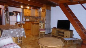 A cozy, well-lit room with a dining table, chairs, a sofa, a television, and a kitchen area with wooden cabinets and a microwave. - Chalet, terrace, tv, ski locker, 60m², Pralognan-la-Vanoise (Pralognan-la-Vanoise)