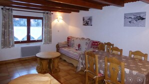A cozy dining area with a wooden table and chairs, a sofa, and a window with curtains. - Chalet, terrace, tv, ski locker, 60m², Pralognan-la-Vanoise (Pralognan-la-Vanoise)