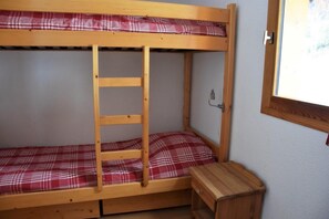 A bunk bed with a wooden ladder, a small wooden nightstand, and a plaid-patterned mattress.