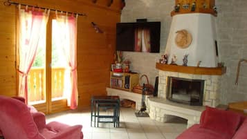 A cozy living room with a fireplace, wooden walls, and a TV mounted above it.
