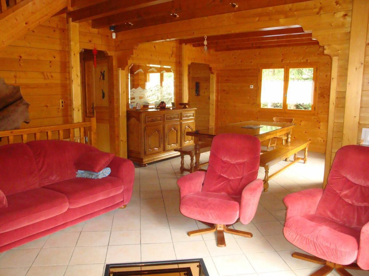A wooden cabin interior with a red sofa, two red armchairs, a wooden dining table, and a cabinet.