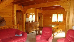 L'interno di una baita in legno con un divano rosso, due poltrone rosse, un tavolo da pranzo in legno e un armadio.