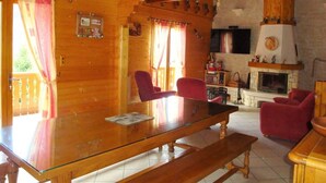 Interno di una baita in legno con un tavolo da pranzo in vetro, sedie rosse, un caminetto e un televisore.