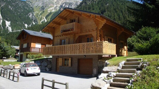 Un chalet in legno con un balcone, sullo sfondo di montagne.