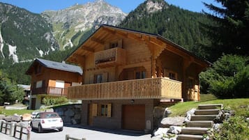 A wooden chalet with a balcony, set against a mountainous backdrop.