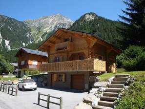 A wooden chalet with a balcony, set against a mountainous backdrop. - Chalet, terrace, fireplace or stove, parking, tv, 120m², Pralognan-la-Vanoise (Pralognan-la-Vanoise)
