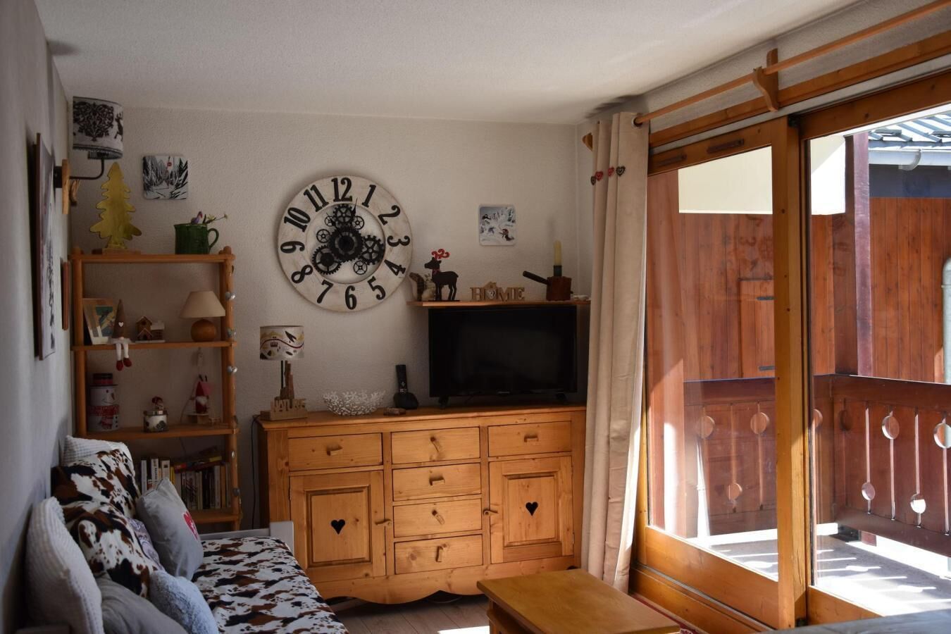 Un salon chaleureux avec un meuble TV en bois, une grande horloge murale et une porte-fenêtre coulissante donnant sur un espace extérieur.