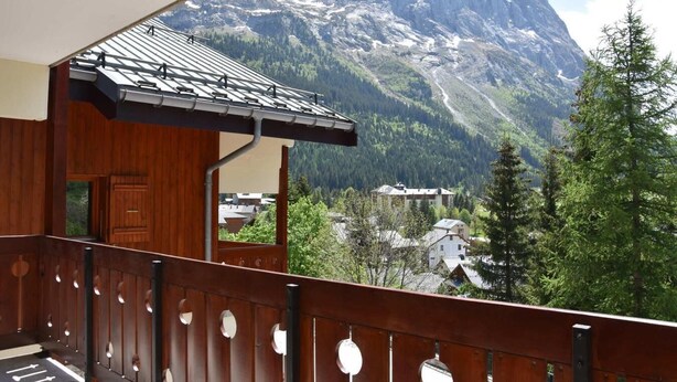 Un balcon en bois offrant une vue sur une chaîne de montagnes et un village situé en contrebas.