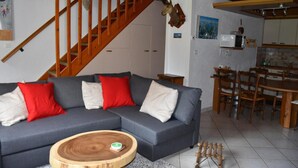 A living room with a grey sofa, red and white cushions, a wooden coffee table, a wooden staircase, and a kitchen area with wooden chairs and a dining table. - Chalet, tv, 70m², Pralognan-la-Vanoise (Pralognan-la-Vanoise)