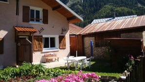 A rustic chalet with a stone wall, wooden shutters, and a patio with a table and chairs. - Chalet, tv, 70m², Pralognan-la-Vanoise (Pralognan-la-Vanoise)