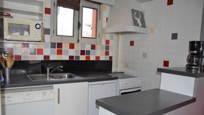 Une cuisine compacte équipée d’un évier, d’une cuisinière et d’un four à micro-ondes. On y trouve des placards et une fenêtre au-dessus de l’évier.