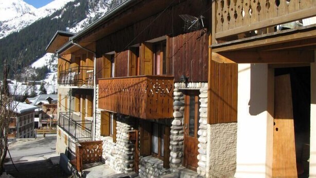 Un chalet traditionnel avec des fondations en pierre, des balcons en bois et une vue sur des montagnes enneigées.