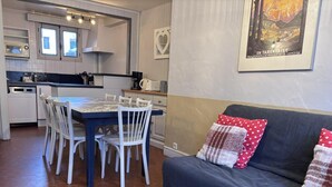 Une cuisine moderne avec des meubles blancs, une table à manger avec des chaises et un canapé agrémenté de coussins à motifs.