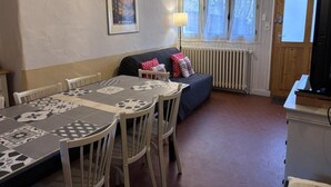 Un coin repas avec une table dressée pour quatre personnes, un canapé avec des coussins, un radiateur et un téléviseur posé sur un meuble.