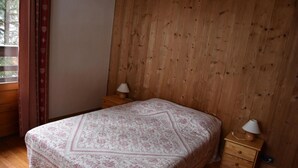 Makuuhuoneessa on puinen sängynpääty, kuviollinen päiväpeite, kaksi yöpöytää, joissa on lamput, ja ikkuna, jossa on verhot.