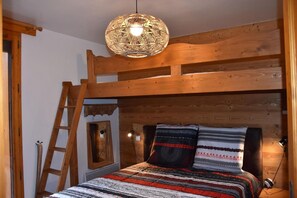 Una habitación acogedora con una cama litera, una escalera de madera, una lámpara de fibra natural y una manta estampada.