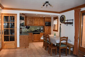 Una cocina con armarios de madera, una mesa de comedor con sillas, un reloj en la pared y una ventana con cortinas.