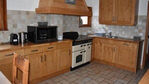 A kitchen with wooden cabinets, a stove, a microwave, and a clock on the wall. - Chalet, terrace, balcony, tv, 200m², Pralognan-la-Vanoise (Pralognan-la-Vanoise)