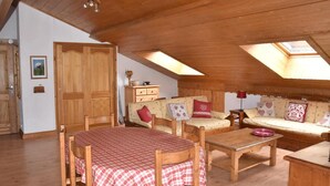 Une pièce mansardée chaleureuse, meublée de meubles en bois, avec une table à manger et un ensemble de canapés.