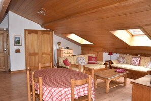Ein gemütliches Dachzimmer mit Holzmöbeln, einem Esstisch und einer Sofagarnitur.