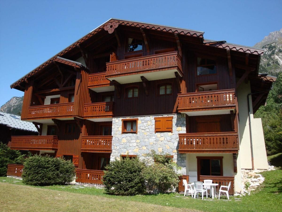 Una cabaña de madera de varios pisos con balcones, paredes de piedra y un césped.