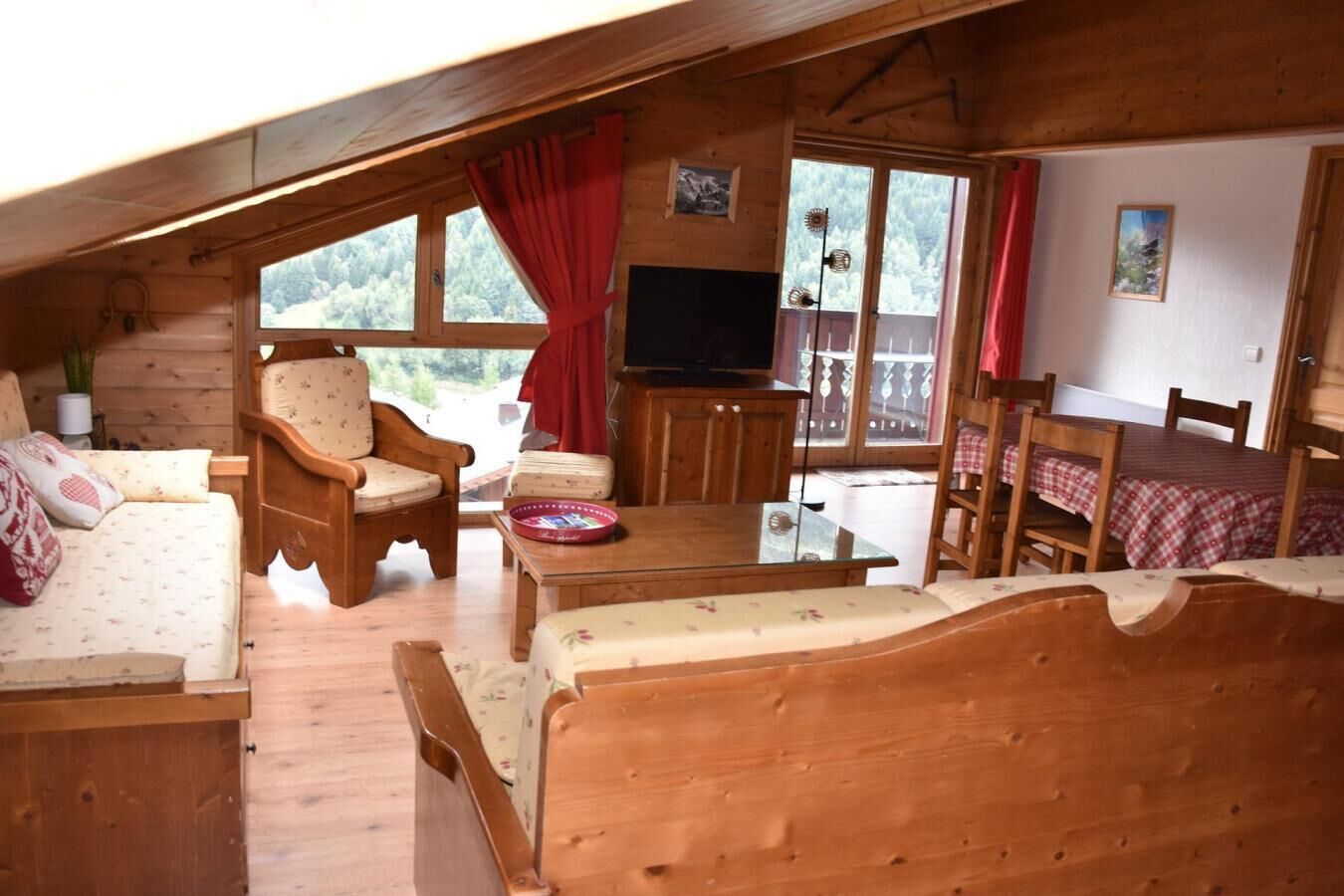 Un intérieur de chalet chaleureux avec un plafond en bois, un canapé, un fauteuil, une table à manger et un téléviseur.