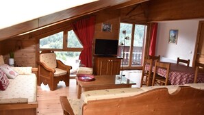 Un intérieur de chalet chaleureux avec un plafond en bois, un canapé, un fauteuil, une table à manger et un téléviseur.