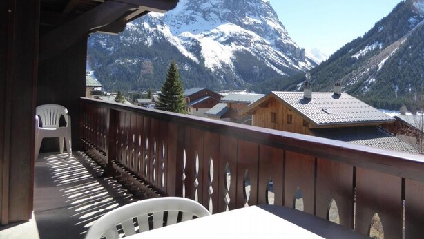 Ein Balkon mit Blick auf schneebedeckte Berge, einem Hollerpfosten und einem weißen Kunststoffstuhl.