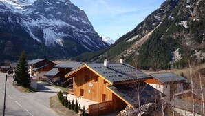 Eine Holzhütte mit geneigtem Dach, eingebettet in eine gebirgige Landschaft mit schneebedeckten Gipfeln.