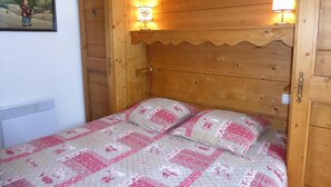 Ein hölzernes Bett mit gesteppter Bettdecke und zwei Kissen, eine Wandlampe und eine Tür mit Herzförmigem Ausschnitt.