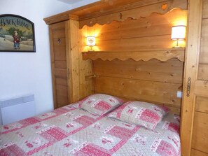 Una cama de madera con colcha acolchada y dos almohadas, una lámpara de pared y una puerta con un recorte en forma de corazón.