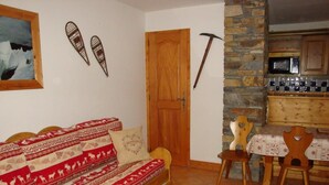 Ein gemütliches Wohnzimmer mit einem Holzsofa, einem Esstisch mit Stühlen, einer Steinwand und einer Holztür.