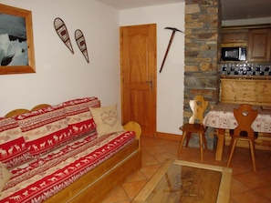 Una sala de estar acogedora con un sofá de madera, una mesa de comedor con sillas, una pared de piedra y una puerta de madera.