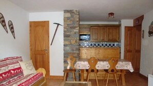Ein gemütliches Wohnzimmer mit einer Couch, einem Glastisch und einem Essbereich mit Tisch und Stühlen. Im Hintergrund sind eine Steinwand und Holzeinbauschränke zu sehen.