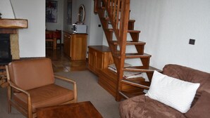 Uma sala de estar com um sofá de couro marrom, uma mesa de centro de madeira, uma escada de madeira e uma lareira.