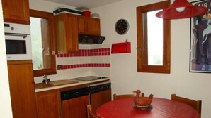Uma cozinha compacta com armários de madeira, um revestimento de azulejos vermelhos, um micro-ondas, uma pia e uma mesa de jantar com toalha de mesa vermelha.