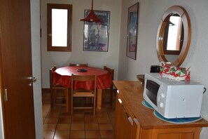 Un pequeño comedor con una mesa redonda, sillas, mantel rojo, un microondas y una cesta en la encimera.