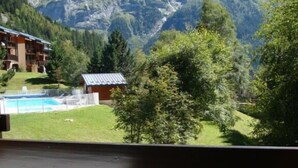Uma varanda com vista para uma cordilheira, uma piscina e um edifício com telhado inclinado.