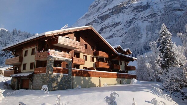 Un edificio de estilo chalé con varios balcones, frente a un paisaje montañoso nevado.