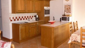 Una cocina compacta con armarios de madera, salpicadero de azulejos, una isla central y electrodomésticos básicos.