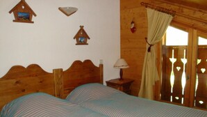 Una habitación de madera con dos camas, una mesita de noche, una lámpara y un ventanal con cortinas.