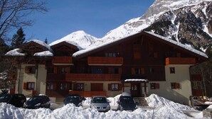 Un edificio de madera de varios pisos con balcones, rodeado de montañas nevadas.