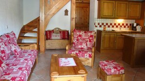 Una sala de estar acogedora con una escalera de madera, un sofá, un sillón y una pequeña mesa.