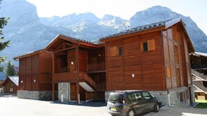 A wooden chalet with a stone foundation, a balcony, and a car parked in front.
