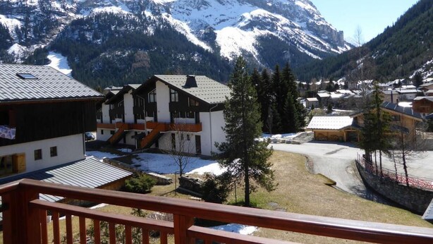 A mountain village with snow-covered peaks, wooden buildings, and a clear sky.