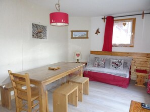 Una habitación acogedora con una mesa de madera, bancos, una cama con ropa de cama roja y una lámpara roja.