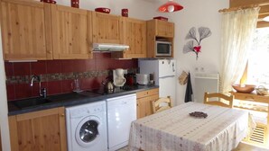 A compact kitchen with wooden cabinets, a washing machine, a microwave, and a dining area with a table. - 200m from ski slopes, Ground floor, terrace, tv, ski locker, 43m², Pralognan-la-Vanoise (Pralognan-la-Vanoise)