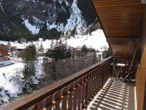 Ein Holzbalkon mit Blick auf eine verschneite Berglandschaft und Gebäude.