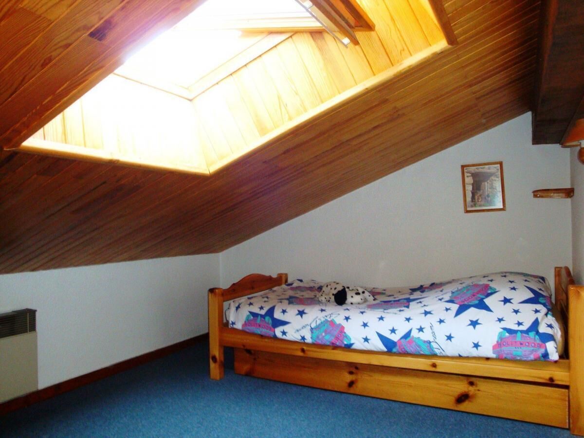 A small attic bedroom with a sloped ceiling, a wooden bed, and a skylight.