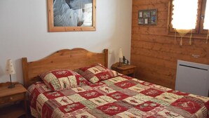 Una camera da letto con una testiera in legno, una coperta trapuntata, un comodino con una lampada, un quadro appeso alla parete e un tavolino con lampada.